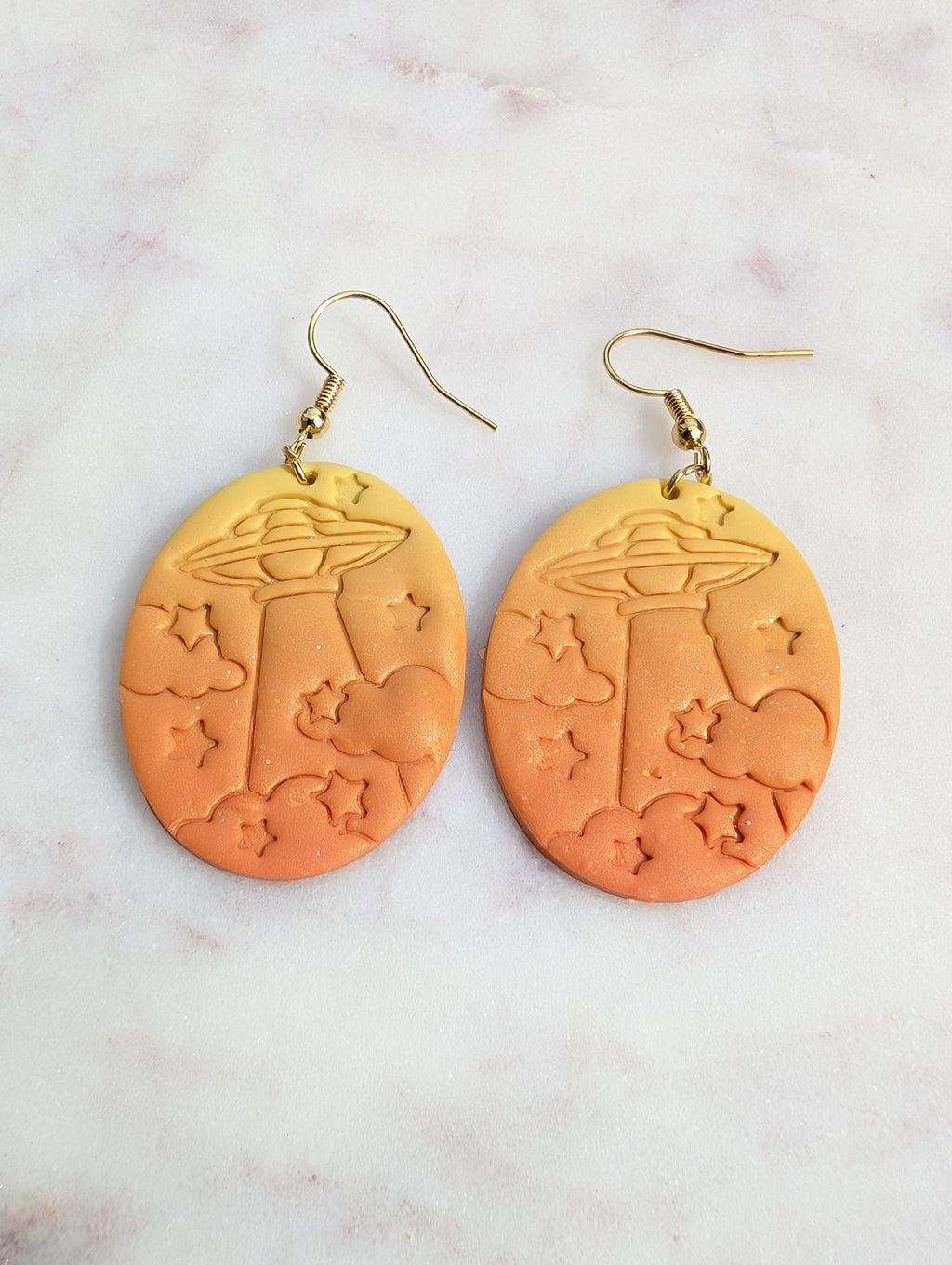 Orange earrings with star and cloud designs on a light gray background