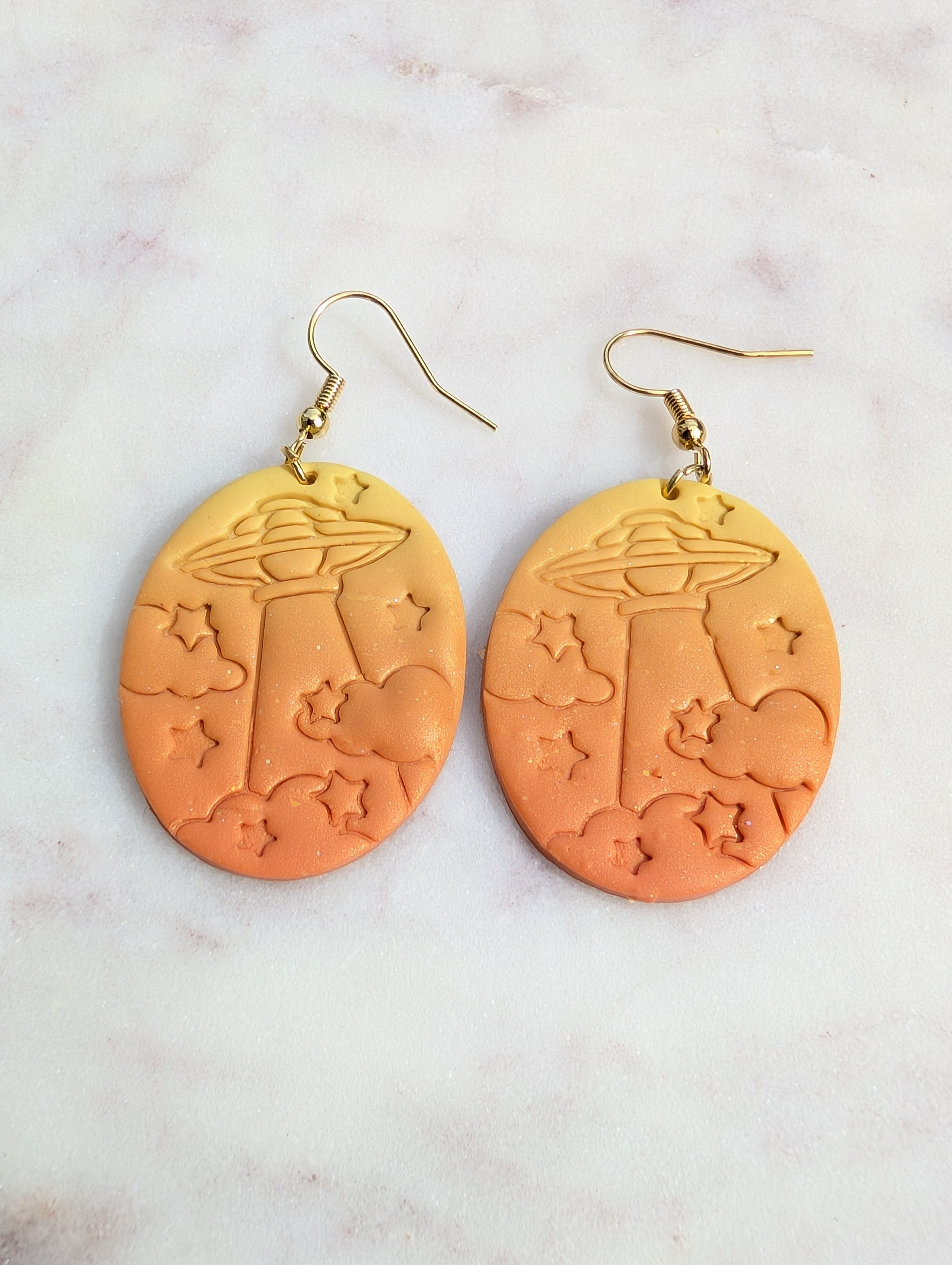 Orange earrings with star and cloud designs on a light gray background